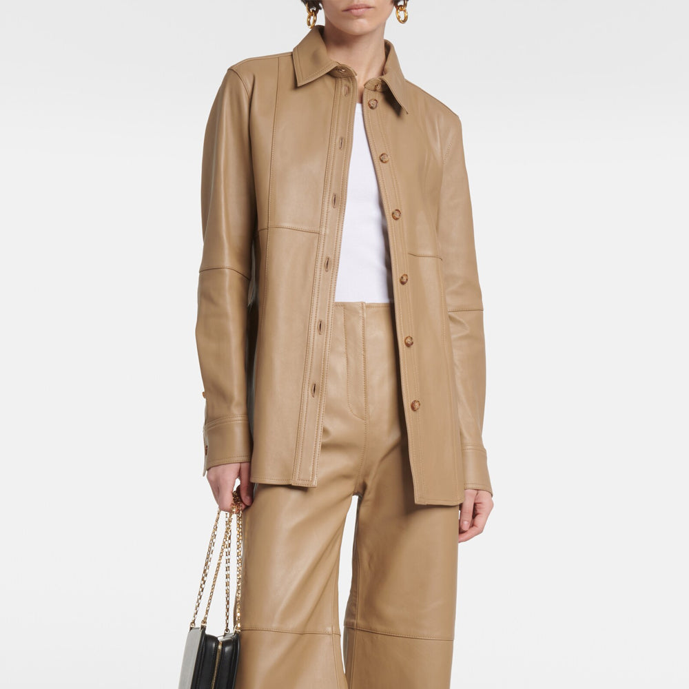 Person wearing a beige leather jacket and pants holding a black handbag on a white background