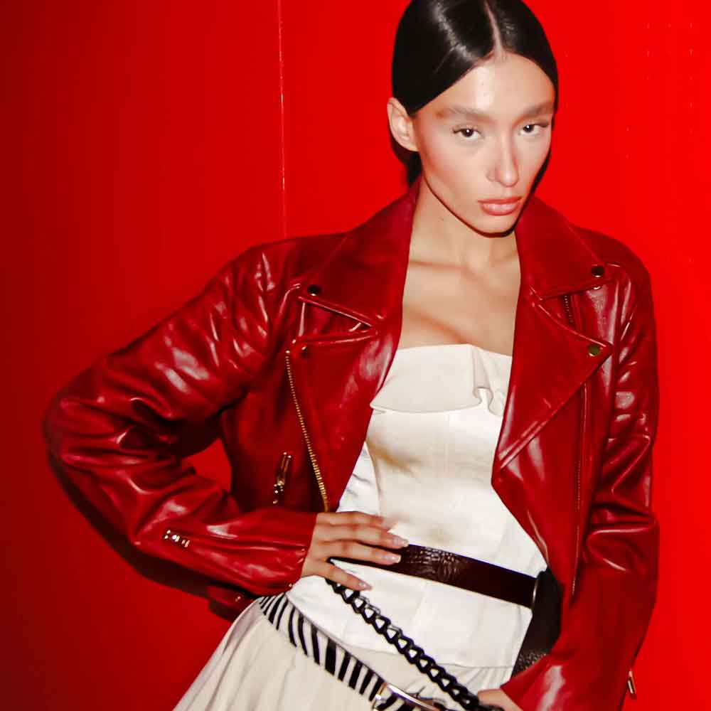 Person wearing a red leather jacket over a white dress on a red background