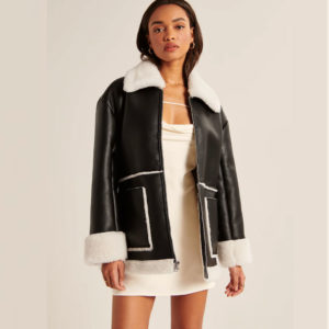 Woman wearing a black leather jacket with white fur trim on a plain background