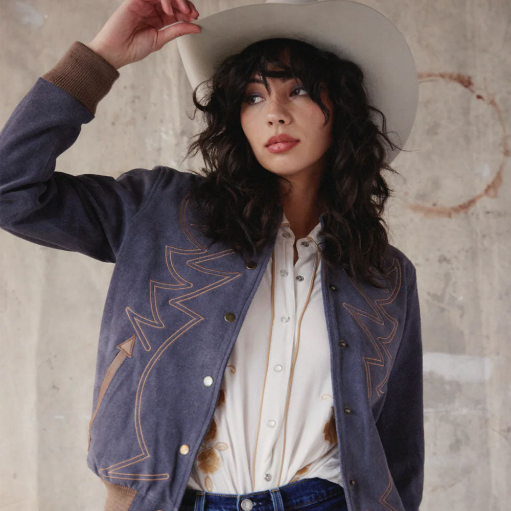 Woman wearing a blue embroidered jacket and white shirt against a textured wall.
