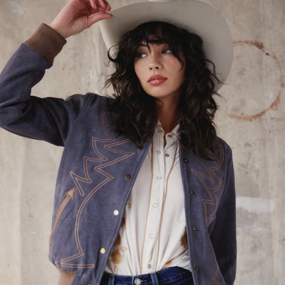 Woman wearing a blue embroidered jacket and white shirt against a textured wall.