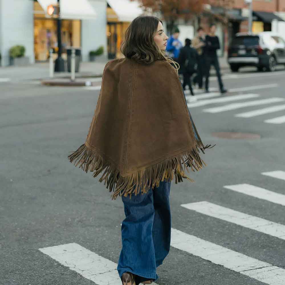 Woman wearing a brown fringed cape walking on a city street.