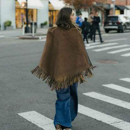 Woman wearing a brown fringed cape walking on a city street.