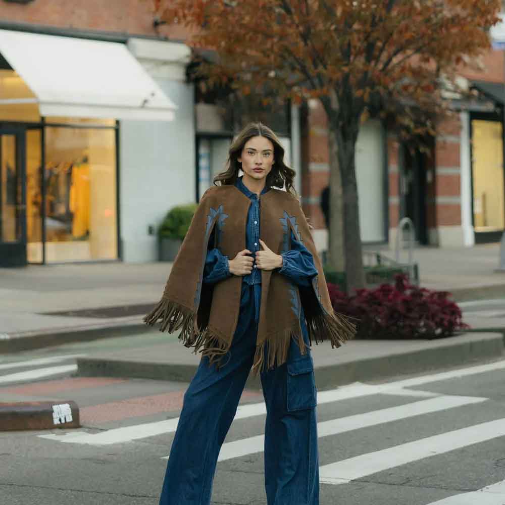 Woman wearing a brown cape and blue outfit on a city street.