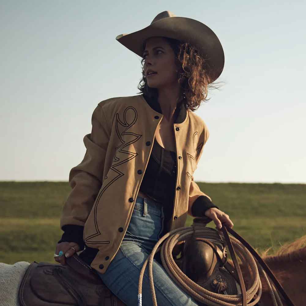 Woman in cowboy hat and jacket holding a lasso in an open field