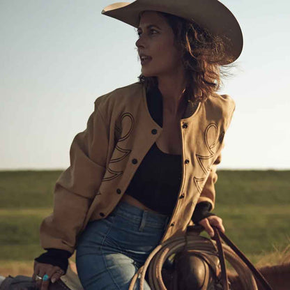 Woman in a beige jacket and cowboy hat holding a lasso in an open field.