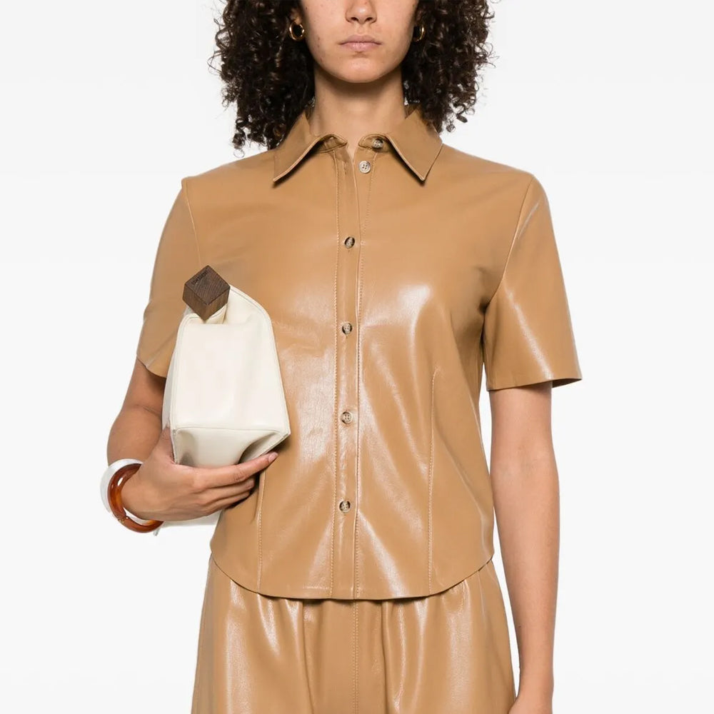 Woman wearing a beige leather outfit holding a white handbag on a white background