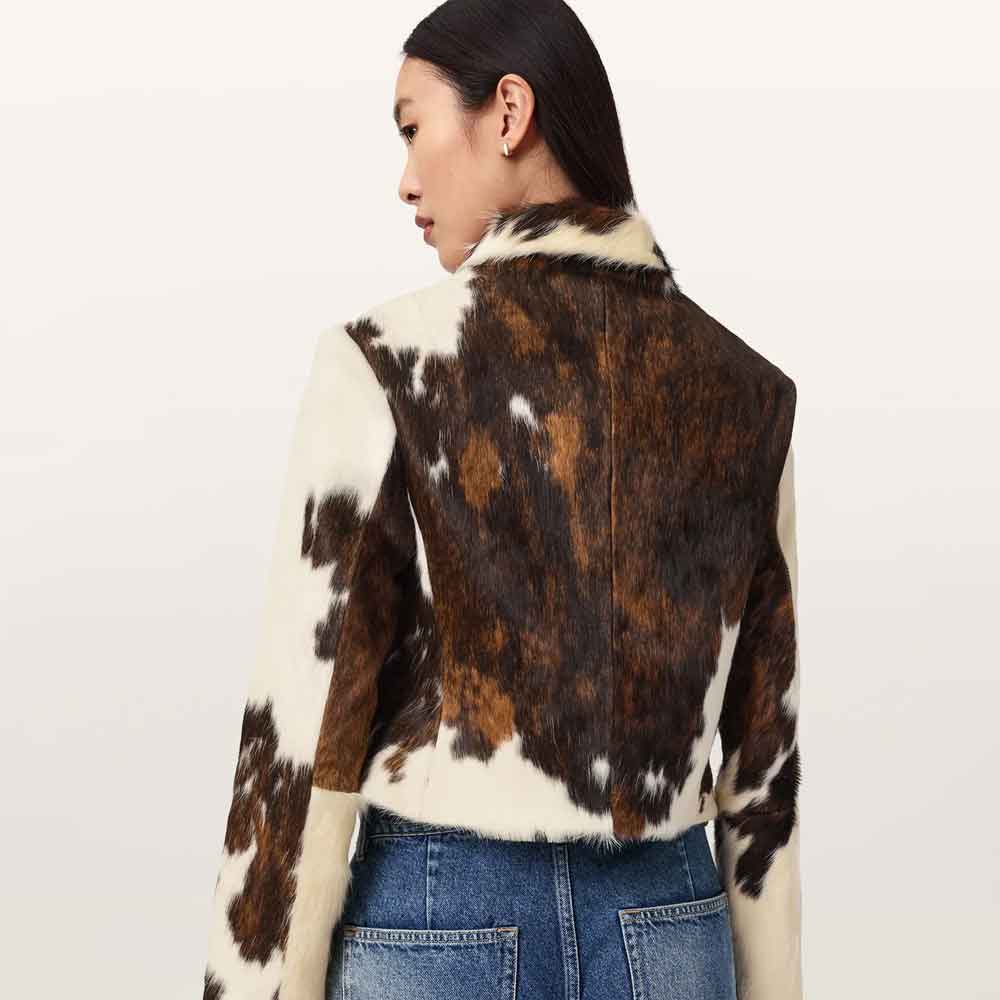 A model shown from the back wearing a cropped cow-print jacket with brown and white patches, paired with blue jeans, against a plain light background.