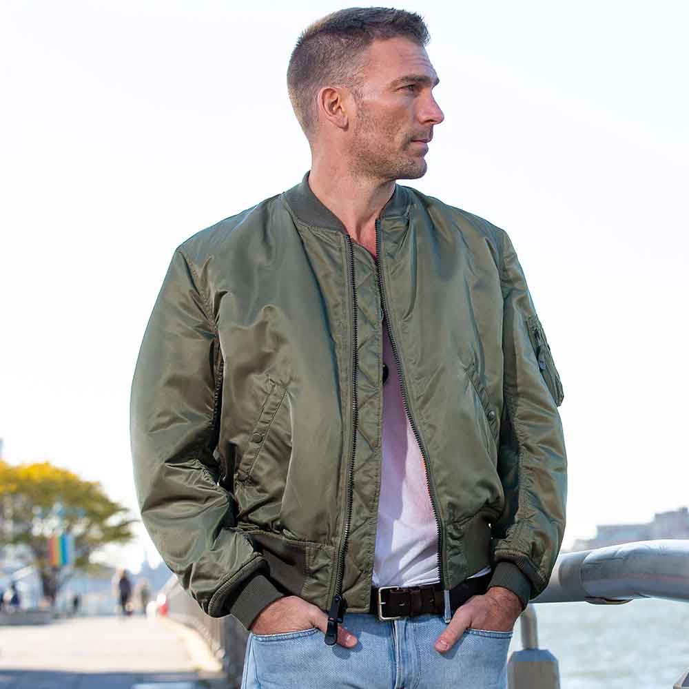 Man wearing a green bomber jacket standing outdoors with a blurred background