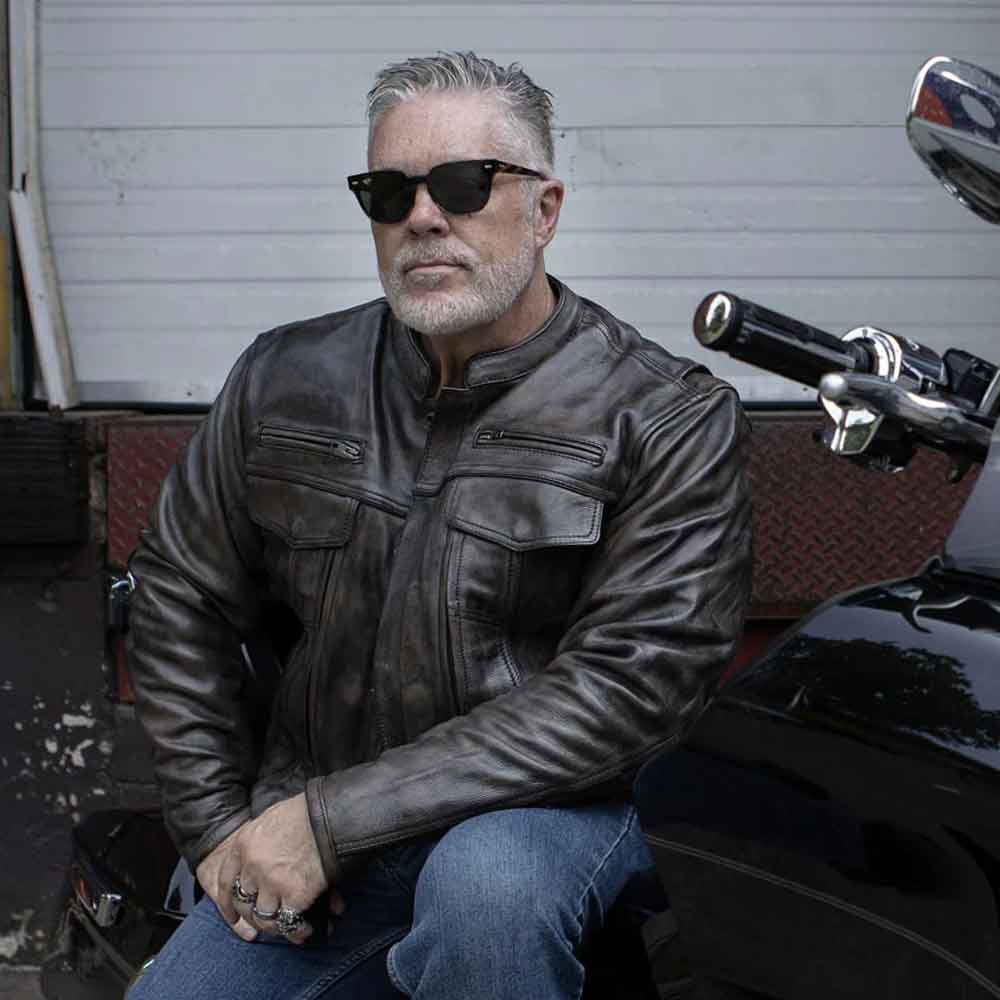 Man wearing sunglasses and a leather jacket sitting on a motorcycle.