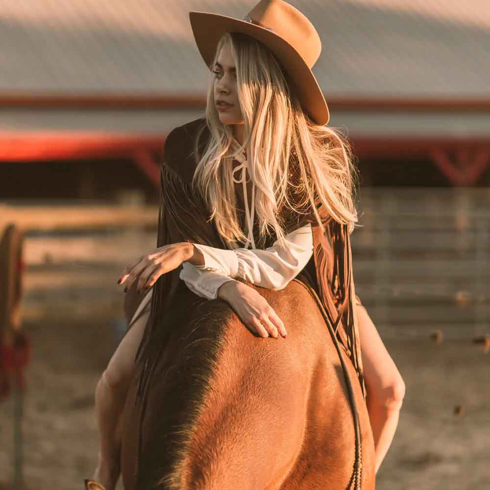 Woman in a cowboy hat riding a horse in a rustic setting