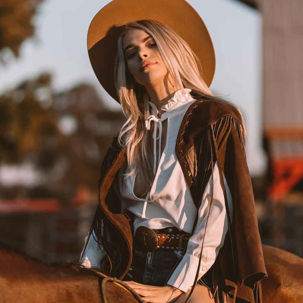 Woman in cowboy attire with a wide-brimmed hat, sitting on a horse.
