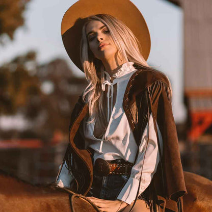 Woman in cowboy attire with a wide-brimmed hat, sitting on a horse.