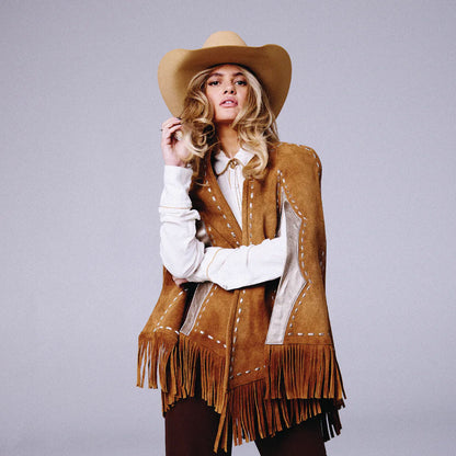 Woman wearing a brown fringed jacket and cowboy hat on a gray background