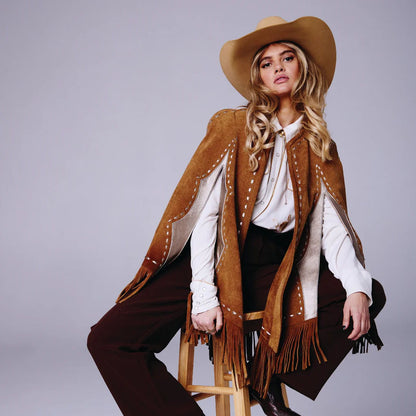 Woman in a cowboy outfit with a brown poncho and hat on a gray background
