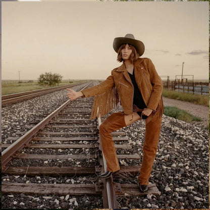 Person in a brown leather jacket and pants sitting on train tracks in a desert setting
