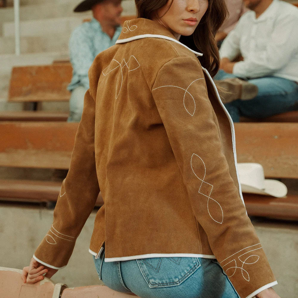 Person wearing a brown suede jacket with white embroidery in an outdoor setting.