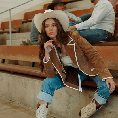 Woman in cowboy hat and boots sitting on bleachers with a man in the background.