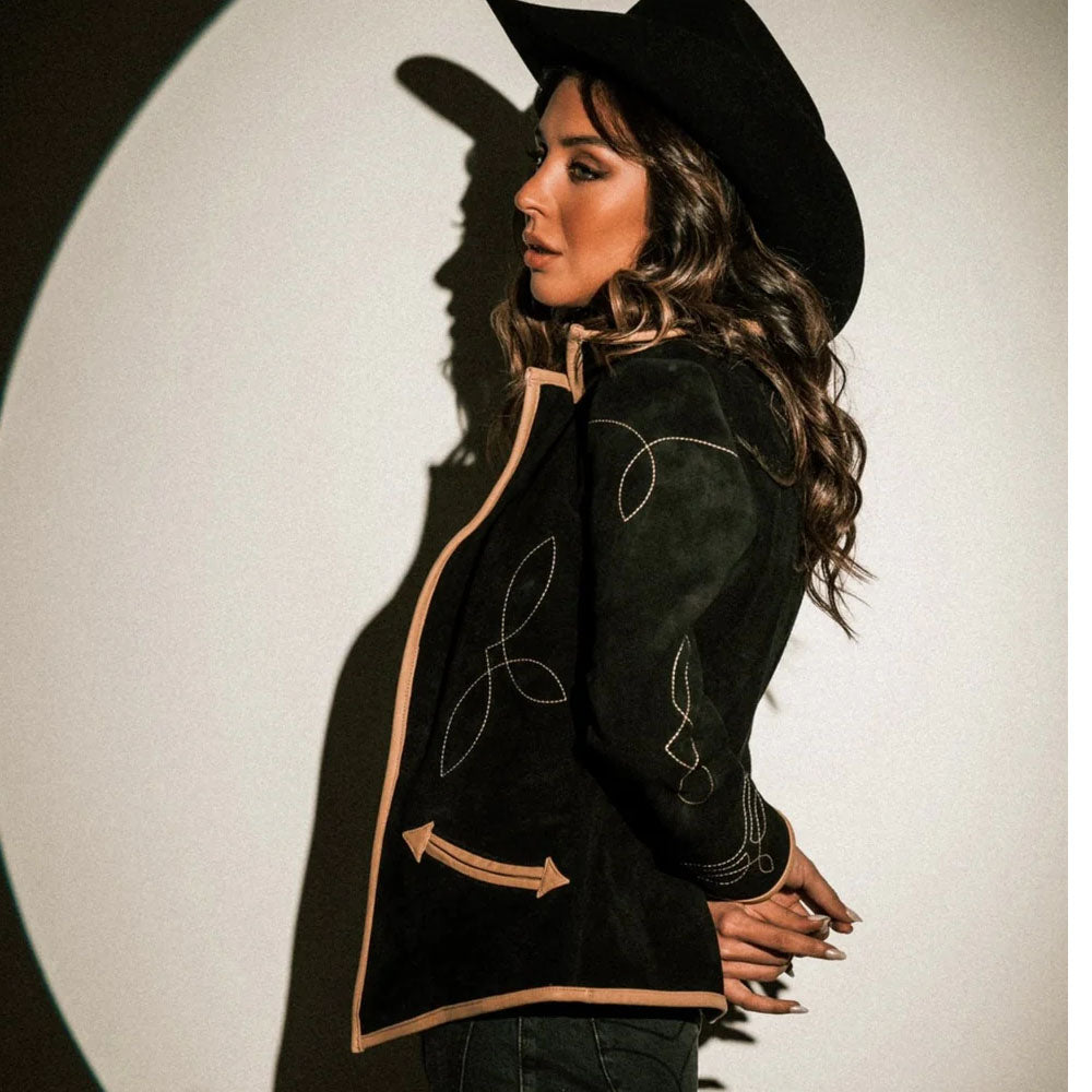 Woman wearing a black jacket with beige embroidery and a black hat against a white background