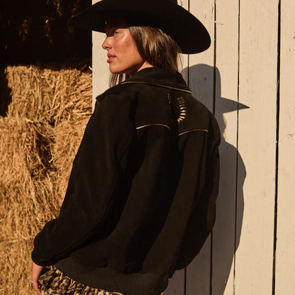 Person wearing a black jacket and hat leaning against a wooden wall with hay bales.