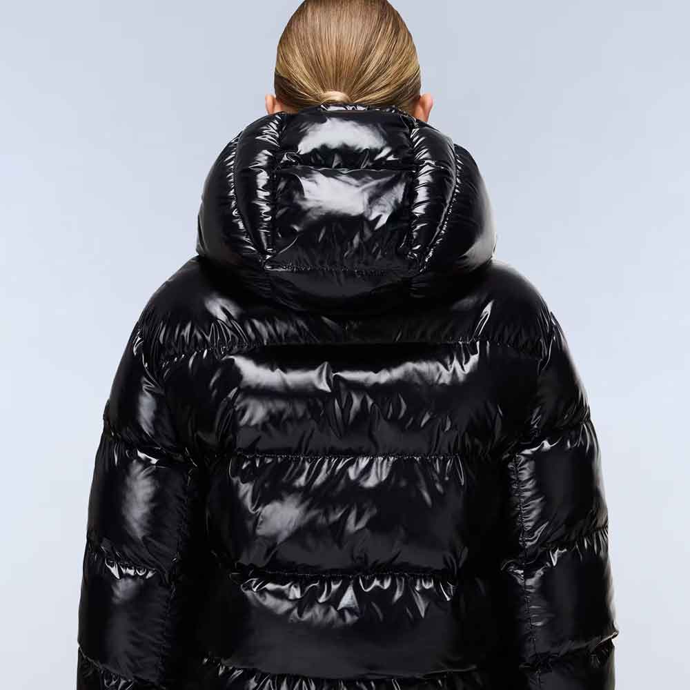 A person viewed from behind wearing a shiny black puffer jacket with a large padded hood, against a light gray studio background.