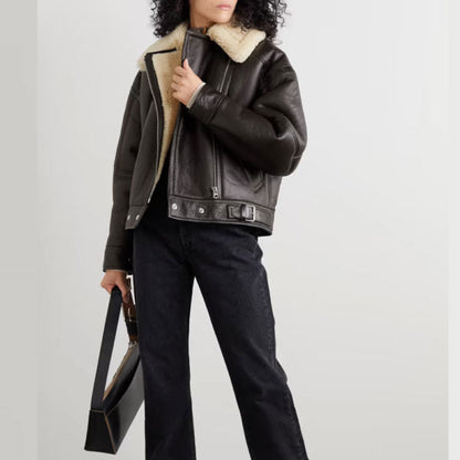 Person wearing a dark leather jacket with shearling collar and holding a black handbag on a light gray background