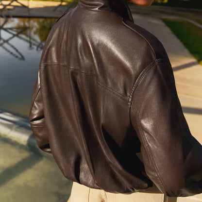 A close-up back view of a person wearing a dark brown leather jacket outdoors near a water feature and walkway.