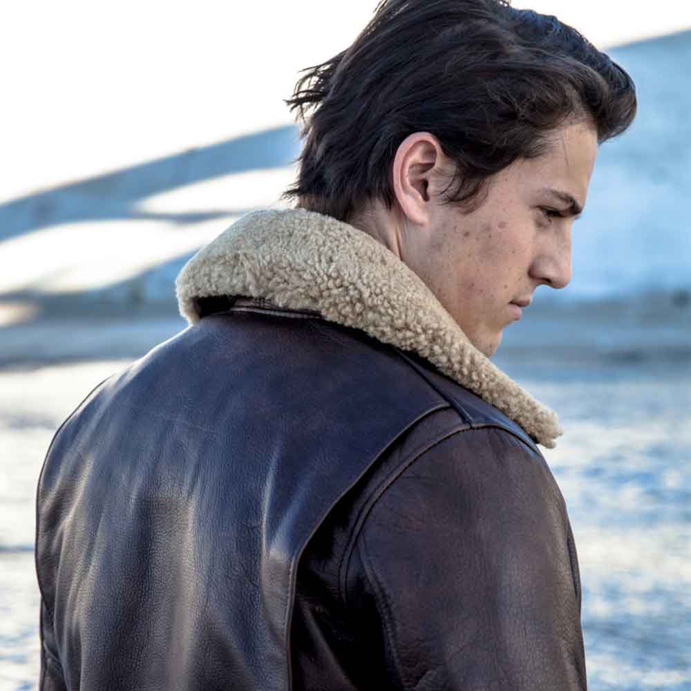Person wearing a leather jacket with a fur-lined hood, standing by a body of water.