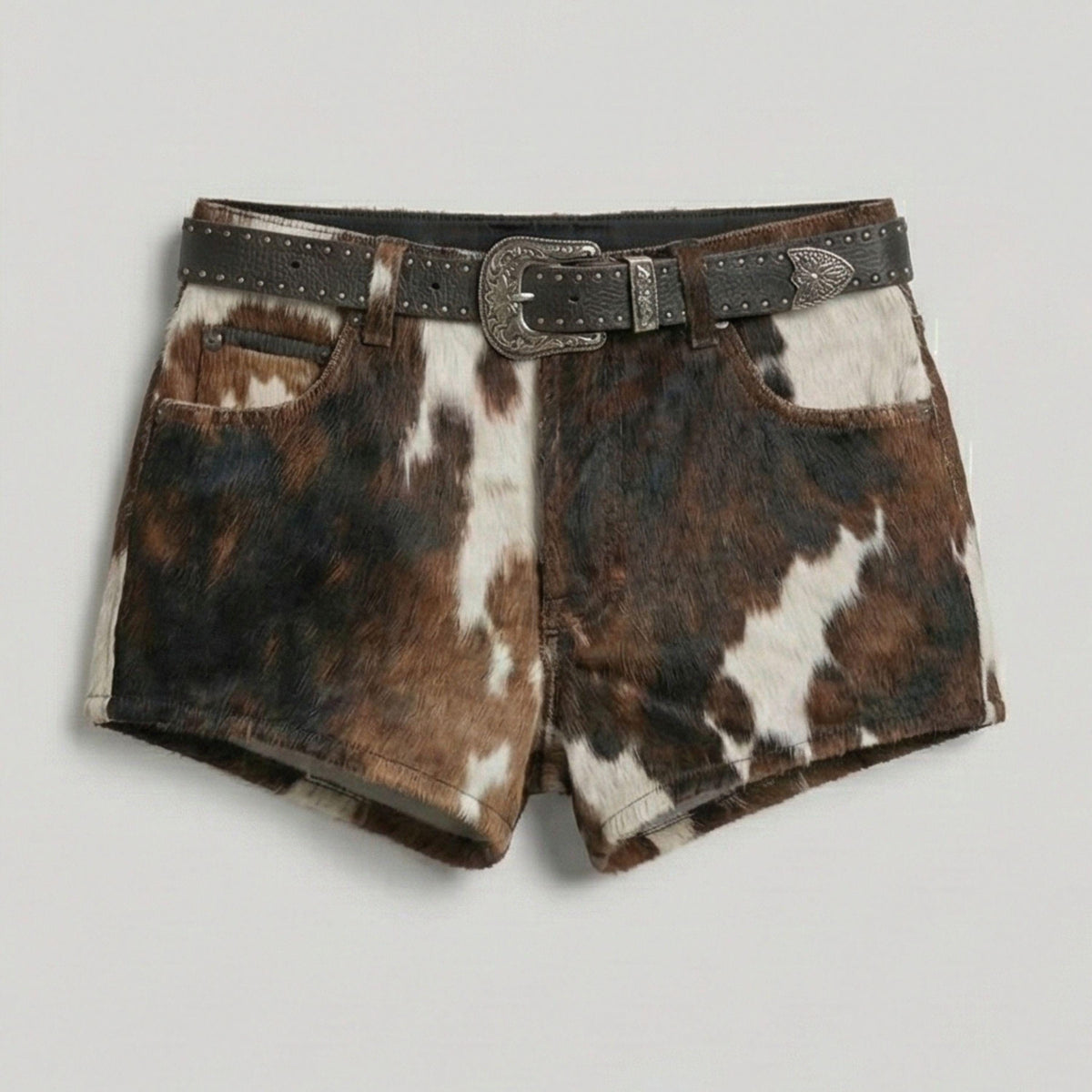 Cow print shorts in brown, black, and white with a matching dark brown studded belt featuring a silver-toned buckle.