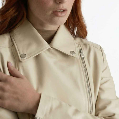 Close-up of a person wearing a light beige moto-style jacket with a collar, snap buttons, and a front zipper, against a plain light background.