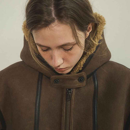 A close-up of a person wearing a brown leather hooded jacket with a tan faux shearling hood and black trim details.