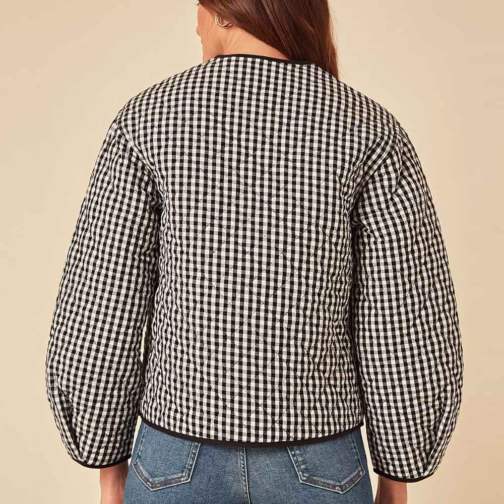 A person shown from the back wearing a black and white gingham quilted jacket with balloon sleeves, paired with blue jeans, against a solid beige background.
