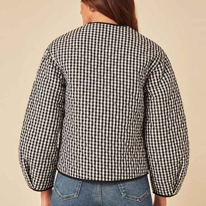 A person shown from the back wearing a black and white gingham quilted jacket with balloon sleeves, paired with blue jeans, against a solid beige background.