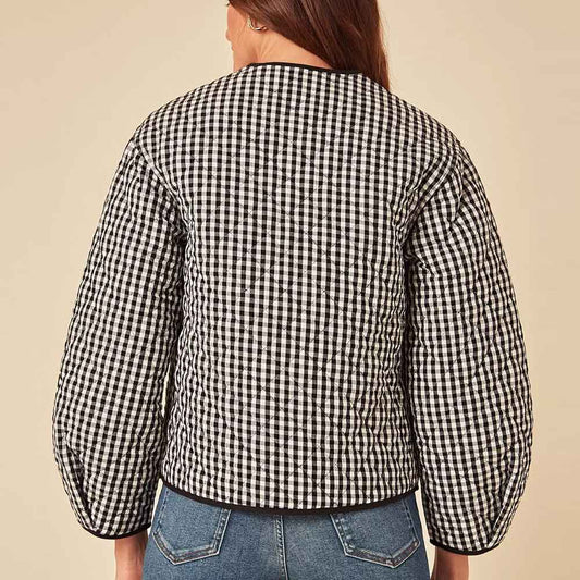 A person shown from the back wearing a black and white gingham quilted jacket with balloon sleeves, paired with blue jeans, against a solid beige background.