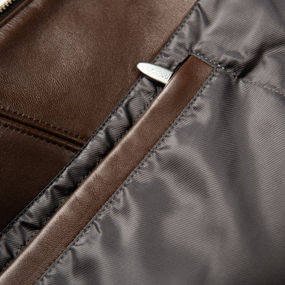 Close-up detail of a brown leather and dark gray nylon bag, showing a silver-tone metal zipper pull engraved with the brand name 'pelle'.
