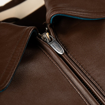 Close-up of a brown leather jacket with a silver metal zipper and a small visible logo on the zipper pull.