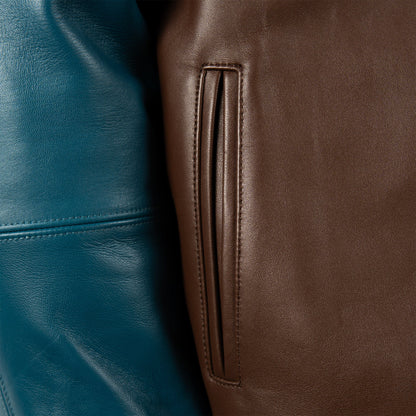 Close-up of a brown leather jacket showing a vertical welt pocket and adjacent stitching, next to a teal blue leather section.