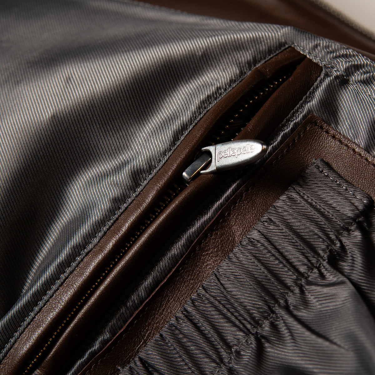 Close-up detail of a brown leather zipper with a silver-tone metal pull engraved with the brand name 'pelle'.
