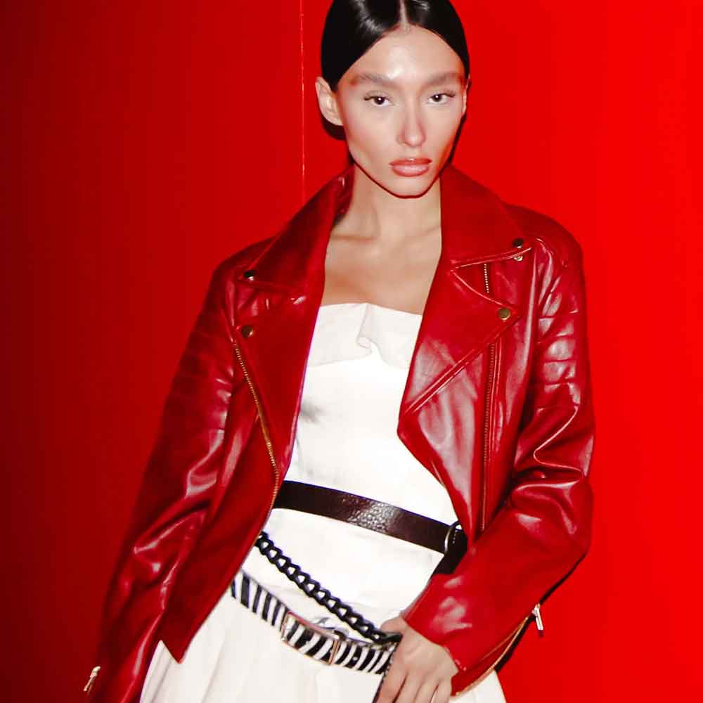 Person wearing a red leather jacket over a white dress with a zebra-striped belt on a red background